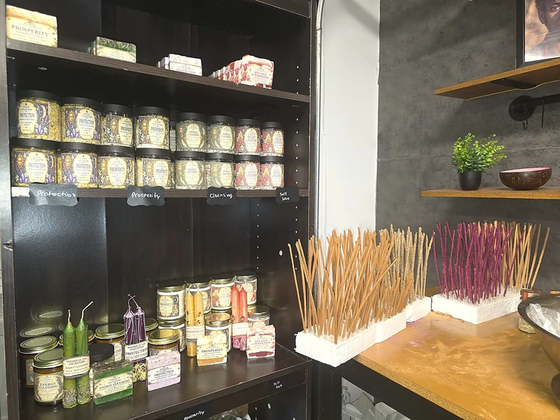 Studio shelves stocked with labeled jars and soaps, beside rows of hand-dipped incense sticks laid out to dry.