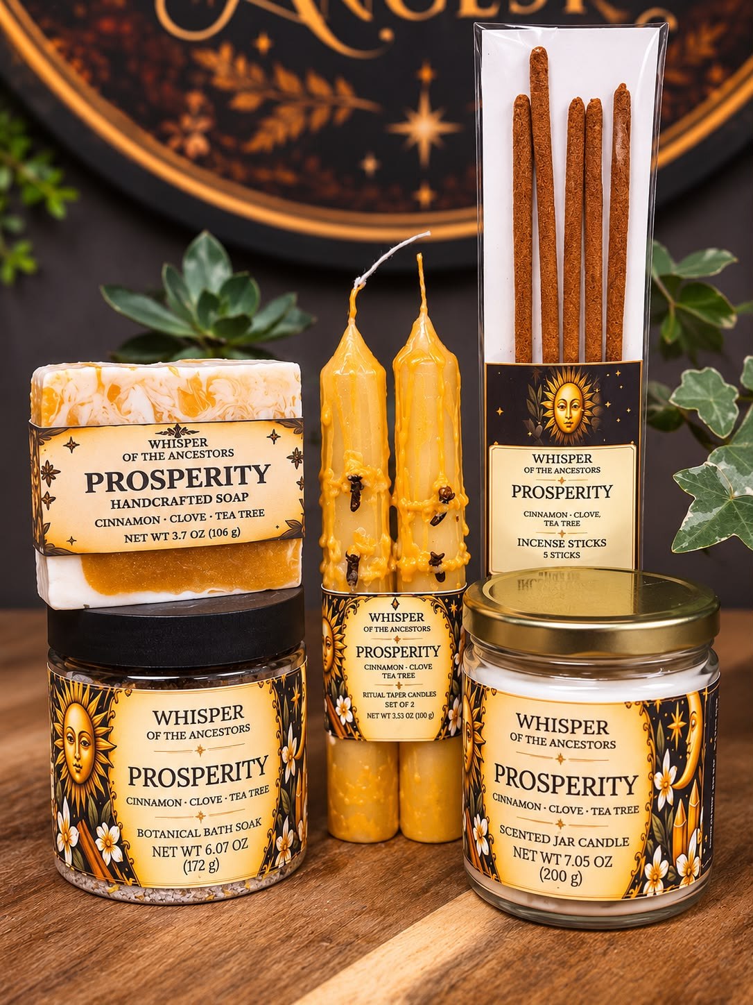 The full Prosperity collection — botanical bath soak in a clear jar with a matte black lid, marbled white-and-gold soap, a pair of golden taper candles with embedded cloves, a white jar candle with a gold lid and five incense sticks in a clear sleeve, all in parchment and black celestial labels, arranged on a wooden table