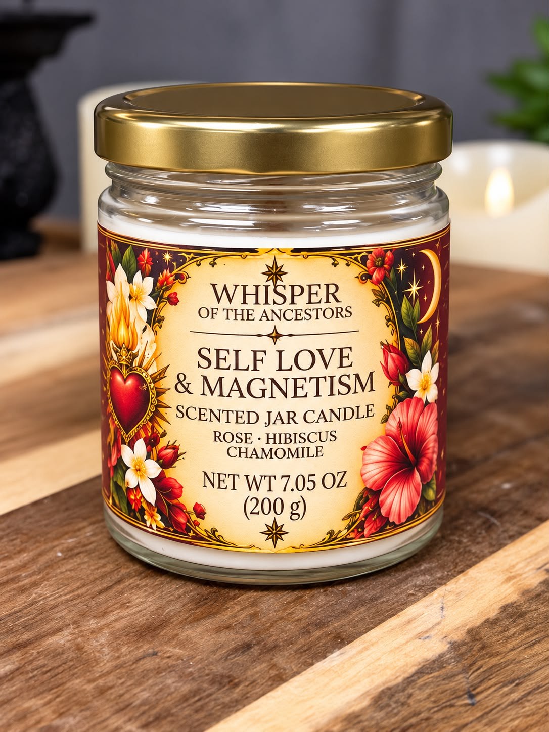 Self Love & Magnetism scented jar candle — white wax in a clear glass jar with a gold lid and a cream label edged in deep red, standing on a striped wooden table