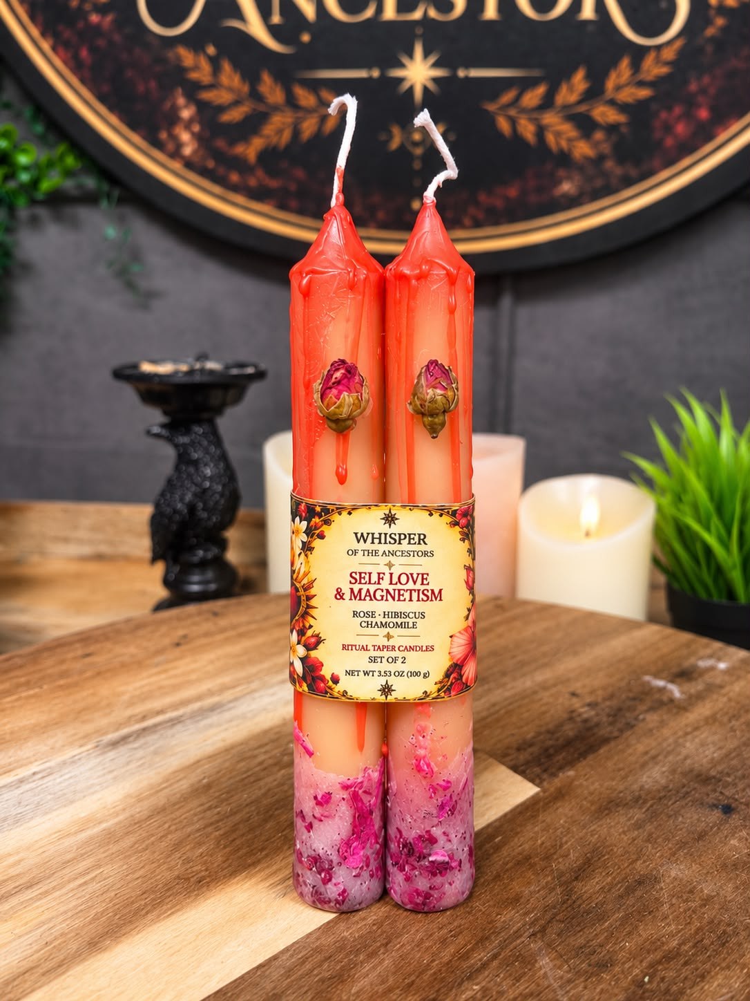 Pair of Self Love & Magnetism ritual taper candles in peach wax with red drips, dried rosebuds near the tops and crushed rose petals around the bases, held together by a cream label band